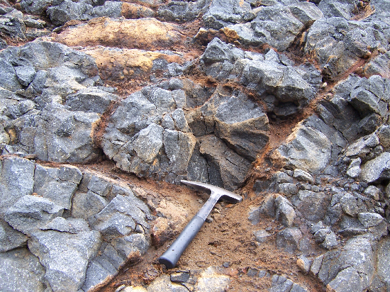 Pillow lavas with a hammer for scale. Notice the radial joints. The pillows are surrounded by brown, altered glass.