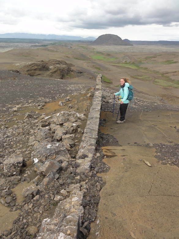 Cara Lembo ('17, Amherst) stands next to a ridge-parallel dike intruding through a tephra cone. Helgafell, a hyalocastite edifice, is in the distance.